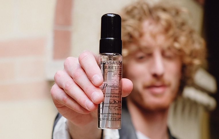 Image of a man with blonde curly hair showing Rossano Ferretti Parma's regenerating Prodigio oil in his hands.