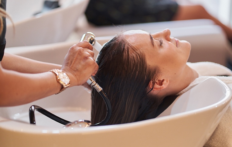 Immagine di una ragazza mentre le stanno lavando i capelli in una postazione da parrucchiera.