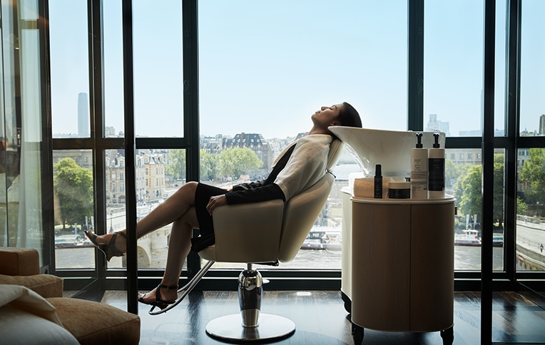 Image of a woman seated at a hair washing station with the Paris skyline behind her.