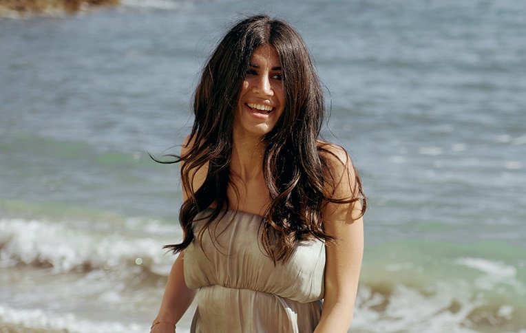 Image of a girl with long, wavy black hair, smiling against a sea background