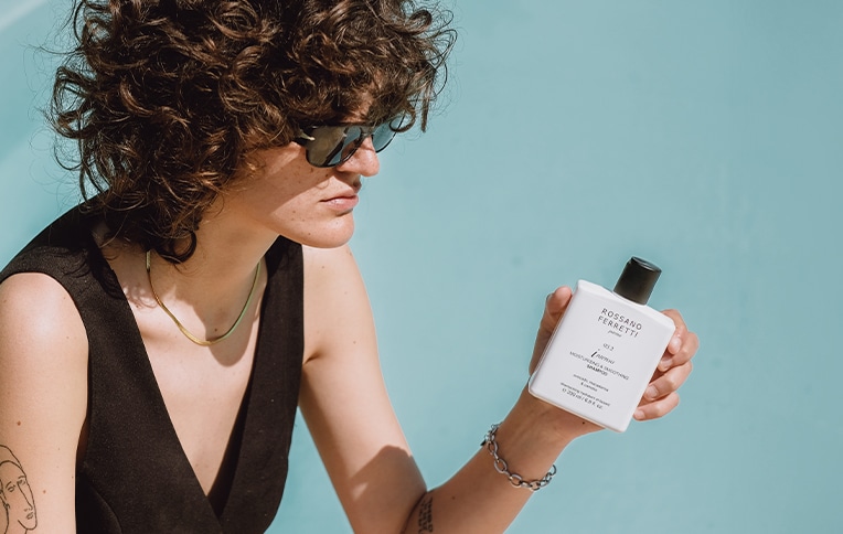 Image of a brunette girl with short, curly hair holding the Intenso smoothing shampoo by Rossano Ferretti Parma in her hand