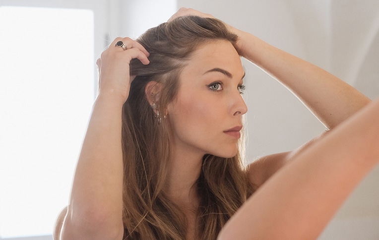 Image of a blonde girl fixing her hair in front of a mirror.