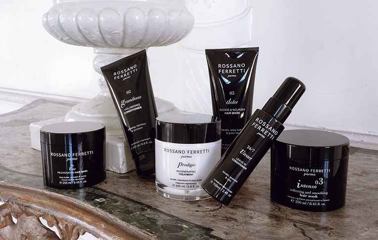 Image of various Rossano Ferretti Parma conditioners and a hair mask placed on a table near a vase