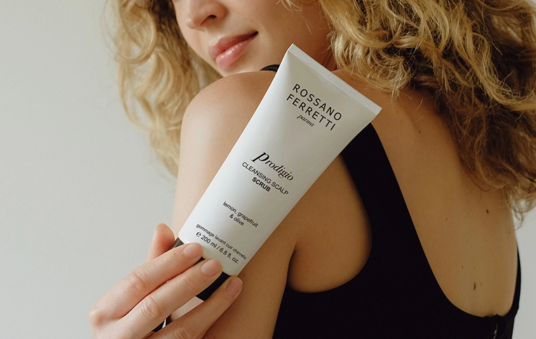 Girl with blonde, curly hair holding the Rossano Ferretti Parma's Prodigio scalp scrub.