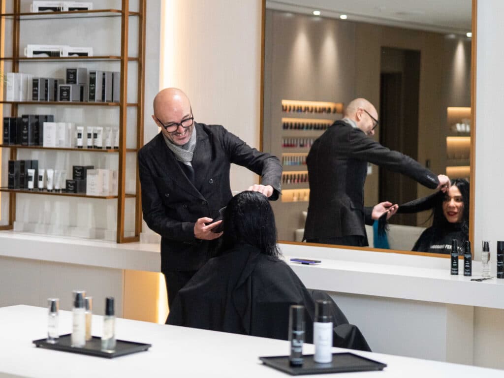 Immagine di Rossano Ferretti mentre sta tagliando i capelli ad una signora.