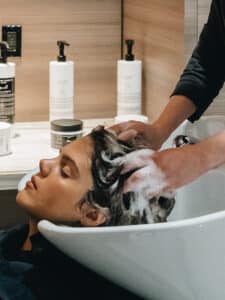 Immagine di una ragazza mentre le stanno lavando i capelli in una postazione da parrucchiera.