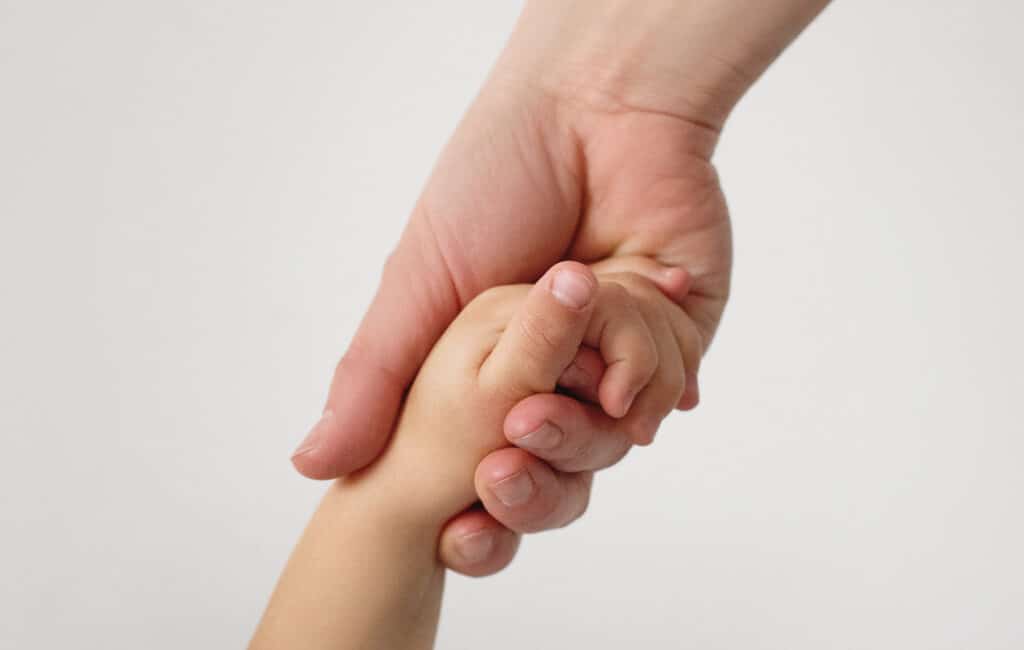 Immagine di una mano di un adulto mentre stringe la mano di un bambino.