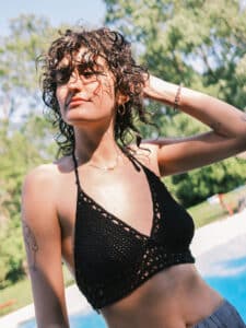 Image of a brunette girl with short, curly hair in a swimsuit near a swimming pool.
