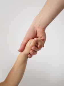 Immagine di una mano di un adulto che tiene per mano una mano di un bambino.