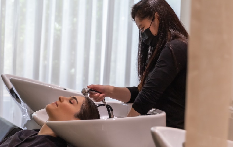 Immagine di una ragazza mentre le stanno lavando i capelli in una postazione da parrucchiera.