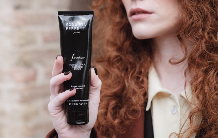Image of a girl with red, curly hair holding the Favoloso Perfect Curls Serum by Rossano Ferretti Parma in her hand.