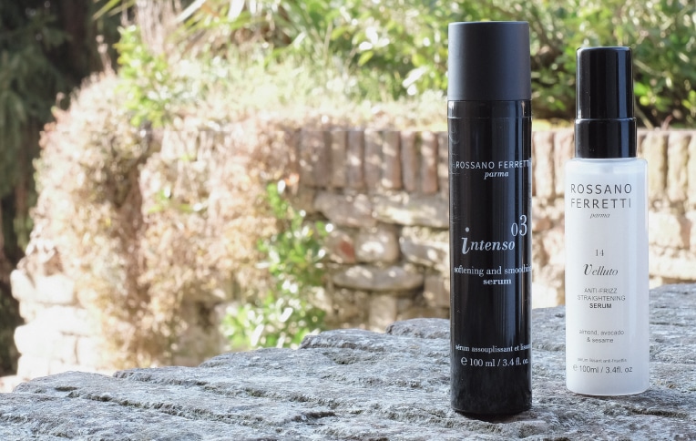 Image of the Intenso softening and smoothing serum and the Velluto straightening, anti-frizz serum by Rossano Ferretti Parma placed on a low wall.