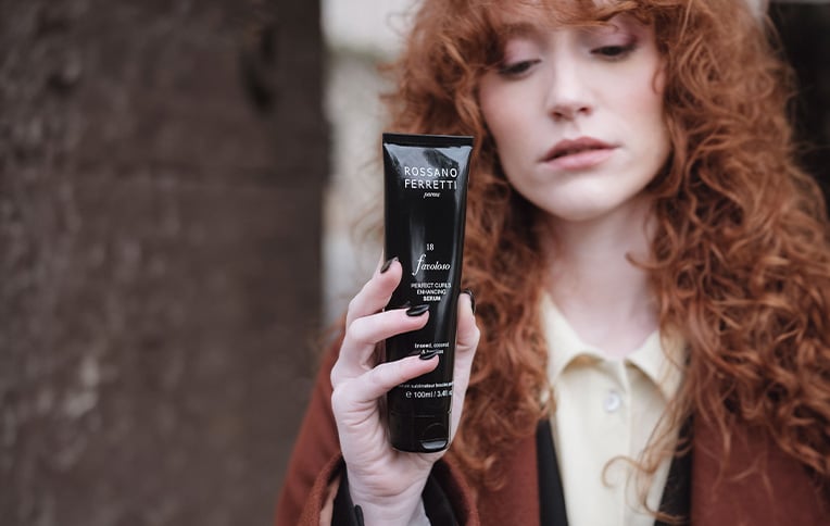 image of a redhead model with curly hair holding and showing Rossano Ferretti Parma's Perfect Curls Serum Favoloso