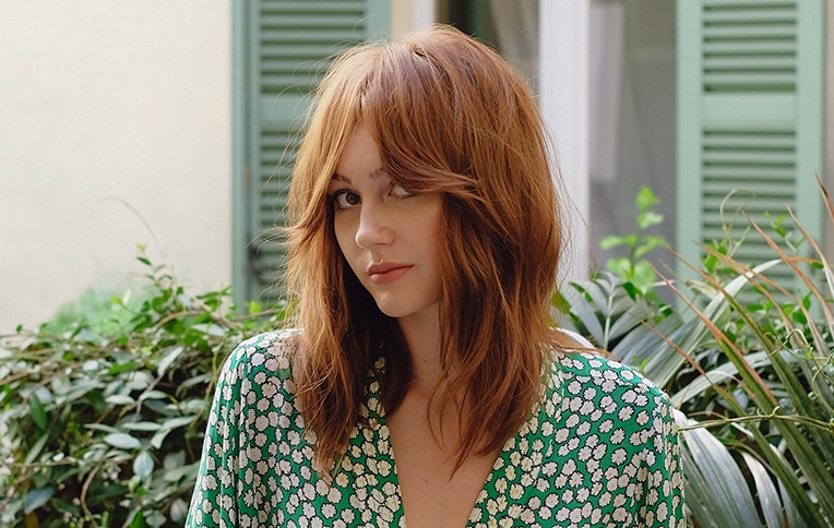 Image of a model with short red hair and curtain bangs, posing sideways.