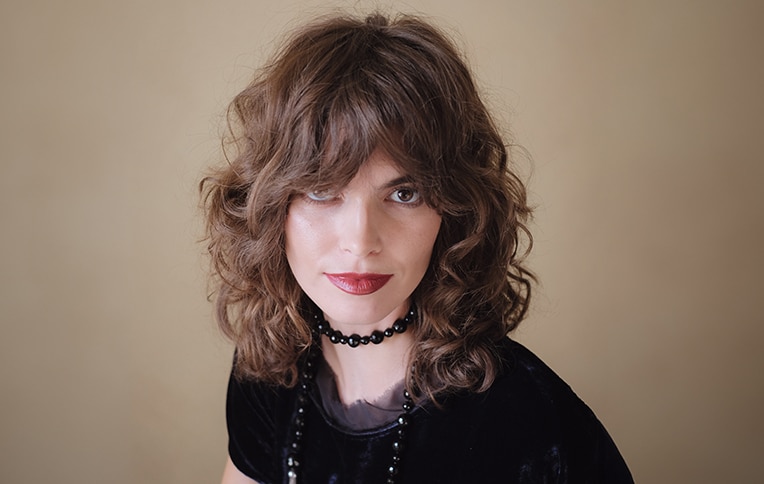 Image of a brunette model with short curly hair and curtain bangs, posing frontally.