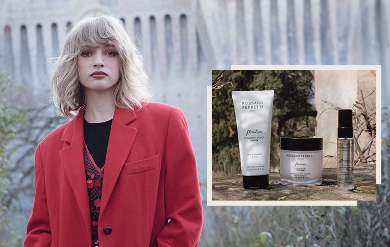 Image of a girl with short blonde hair with the products from the Prodigio line by Rossano Ferretti Parma. Exfoliating scalp scrub, Prodigio regenerating treatment, and Prodigio hair supplement oil