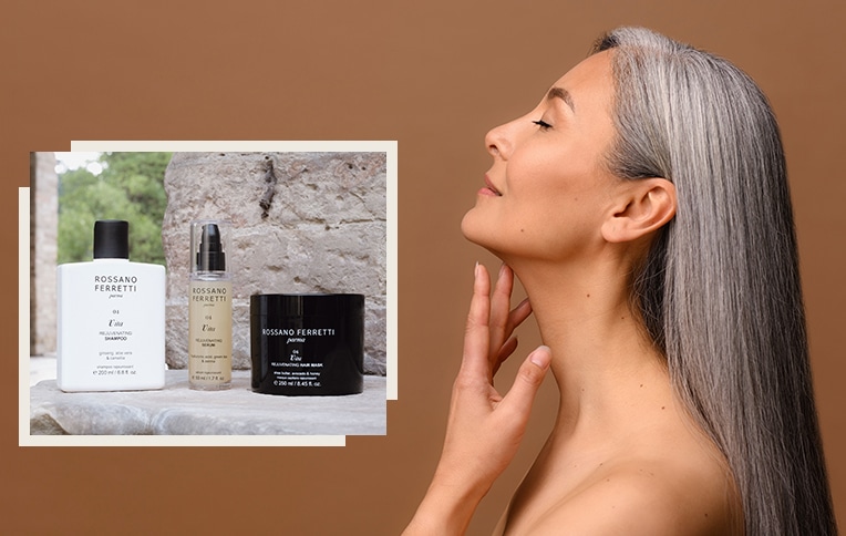 Image of a mature woman with long grey hair with the products from the Vita line by Rossano Ferretti Parma. Shampoo, mask, and Vita rejuvenating serum.