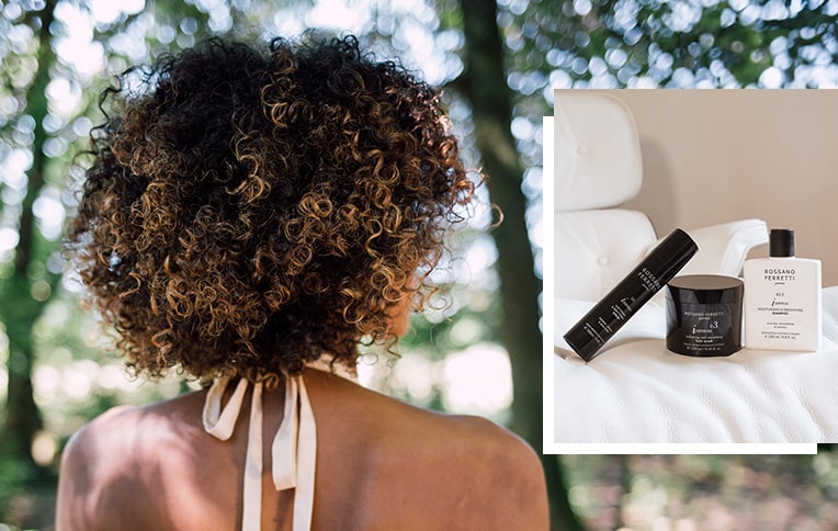 Image of a brunette model with short, coily, voluminous afro hair, with the Intenso smoothing routine with the moisturising & smoothing shampoo, the softening & smoothing mask and the softening & smoothing serum.