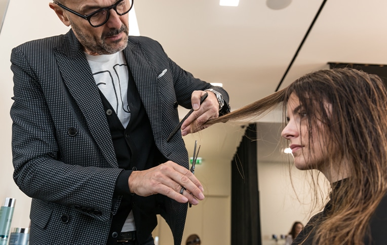 Immagine di Rossano Ferretti mentre taglia i capelli a una cliente.