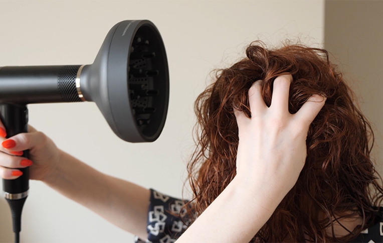 Girl with red and curly hair while drying her hair with a diffuser.