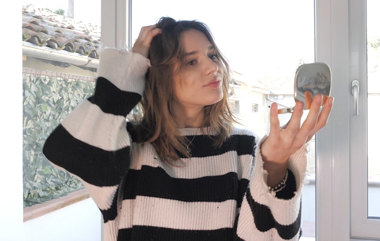 Brunette girl with short hair adjusting her hair in front of a small mirror.