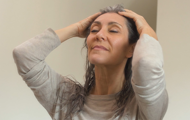 A woman with grey hair massaging her scalp with her hands.