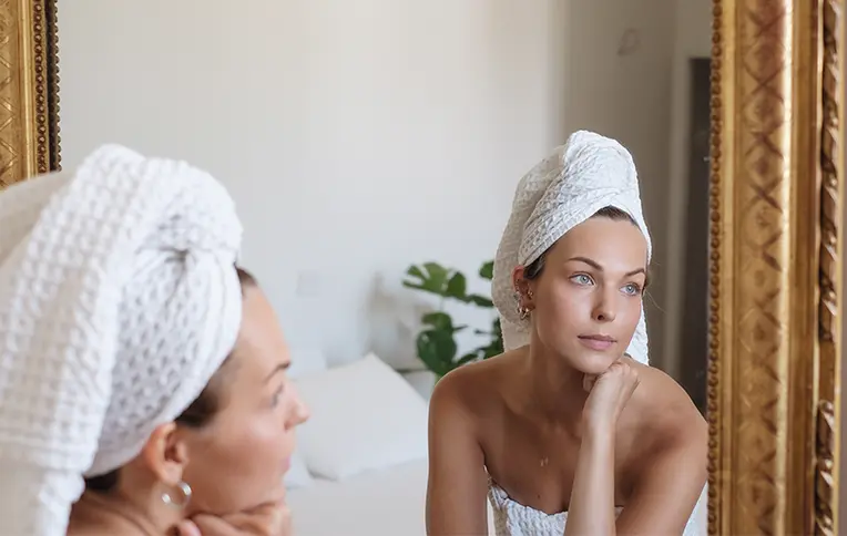 Una donna con un asciugamano avvolto tra i capelli, che si guarda allo specchio.