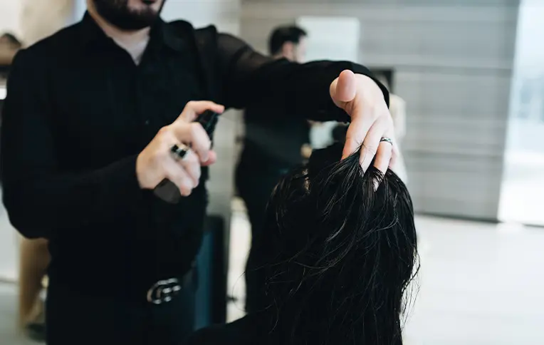 Hairstylist applying a hair spray on a client.