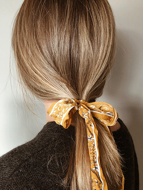 Image of a blonde girl seen from behind with a ponytail and a colorful bow.