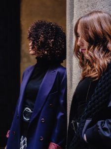 Image of two girls side by side. One of them with very curly afro dark hair and the other with long, wavy, auburn hair.