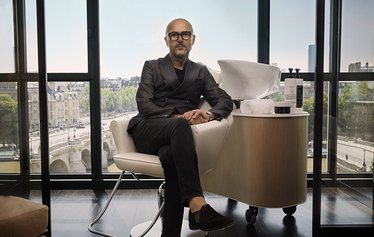 Image of Rossano Ferretti seated on a chair with the Paris skyline in the background.